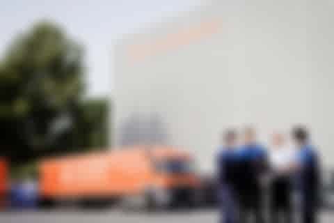 One man explaning Orange truck and group of four people in front of the high rack